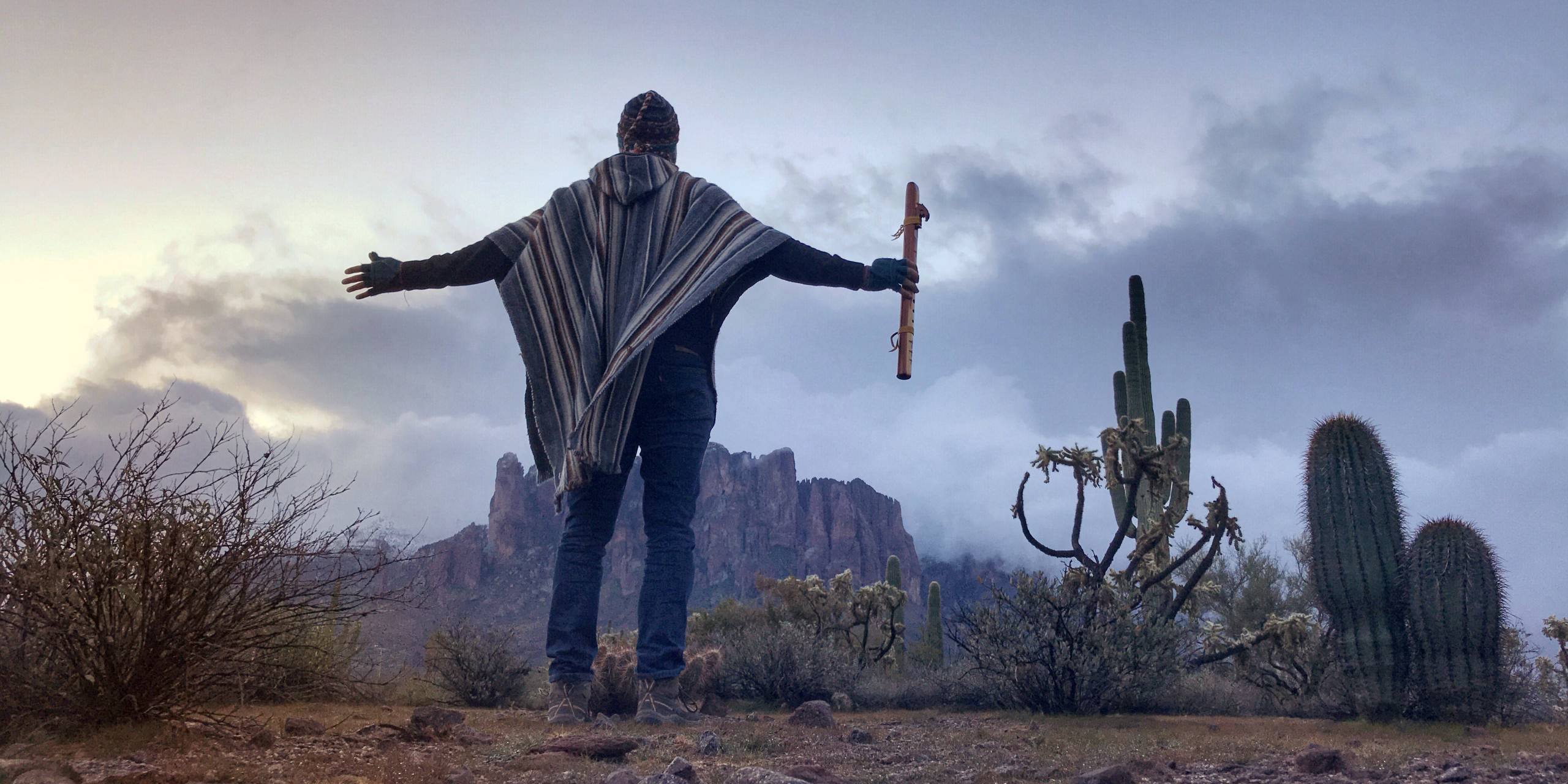 A person standing with both arms open toward a range of mountains.